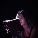 A woman absorbed in a book, illuminated by focused light, creating a dramatic effect.