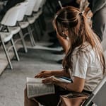 Focused woman reading a book in an academic setting with others in the background.