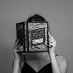 Black and white portrait of a woman reading 'The Gothic Tales of H.P. Lovecraft' in a studio setting.