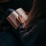 A young woman reading a book in a cozy indoor setting by the window.