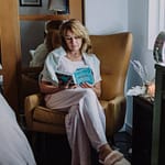 A woman sits in a cozy armchair indoors, enjoying a peaceful reading moment.