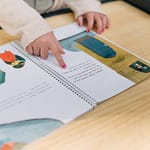 A child interacts with an illustrated book, focusing on the tactile experience of reading.
