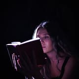 A woman absorbed in a book, illuminated by focused light, creating a dramatic effect.