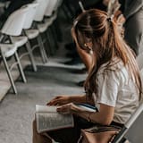 Focused woman reading a book in an academic setting with others in the background.