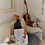 Woman relaxing on a sofa reading a book with an acoustic guitar in the background.