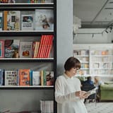 Young woman reading by a bookshelf in a contemporary bookstore setting.