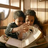 Two children reading a book together on a cozy couch by the window.