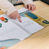 A child interacts with an illustrated book, focusing on the tactile experience of reading.