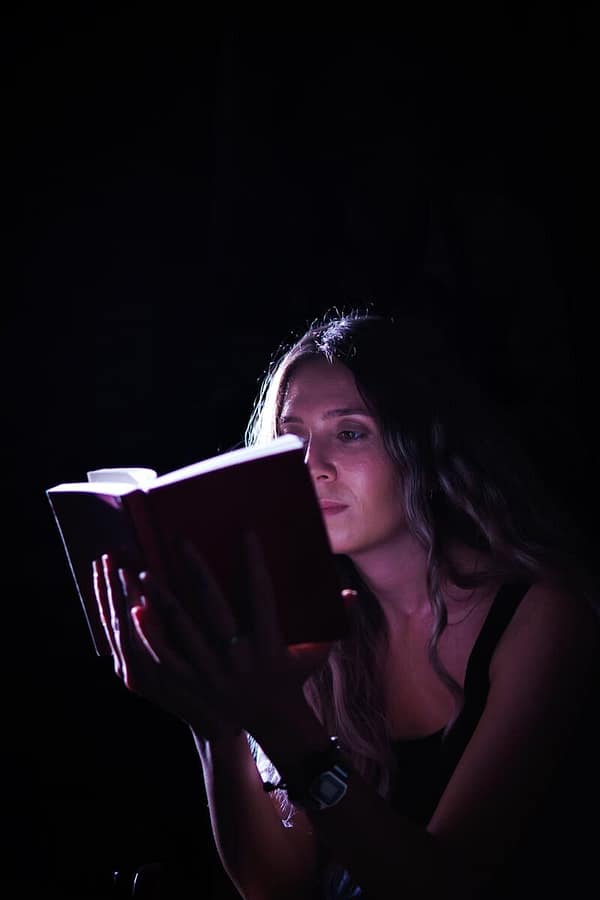 A woman absorbed in a book, illuminated by focused light, creating a dramatic effect.