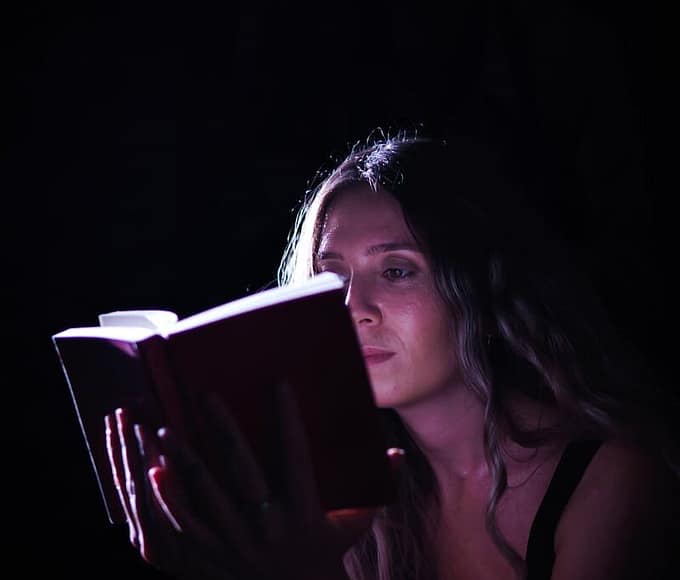 A woman absorbed in a book, illuminated by focused light, creating a dramatic effect.