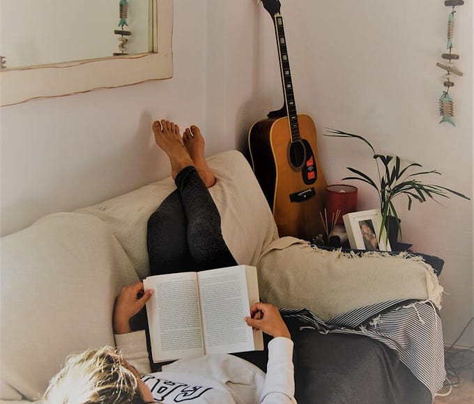 Woman relaxing on a sofa reading a book with an acoustic guitar in the background.