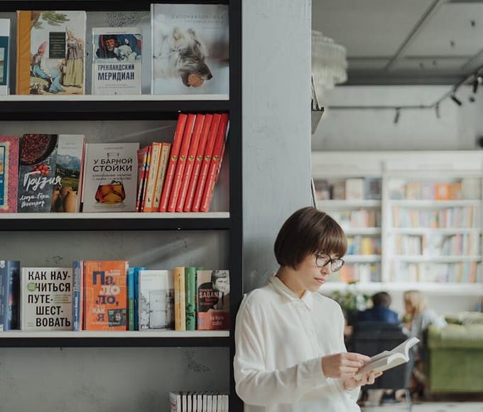 Young woman reading by a bookshelf in a contemporary bookstore setting.