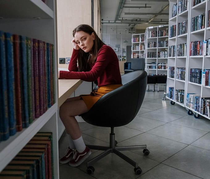 Teenage girl sitting and reading in a contemporary library. Bookshelves line the room.