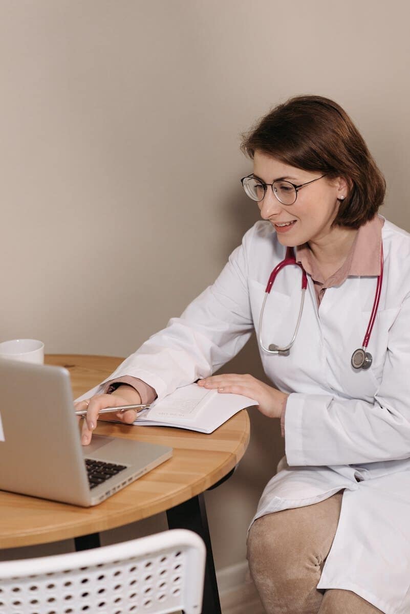 Female doctor using a laptop while sitting at a desk with notes.